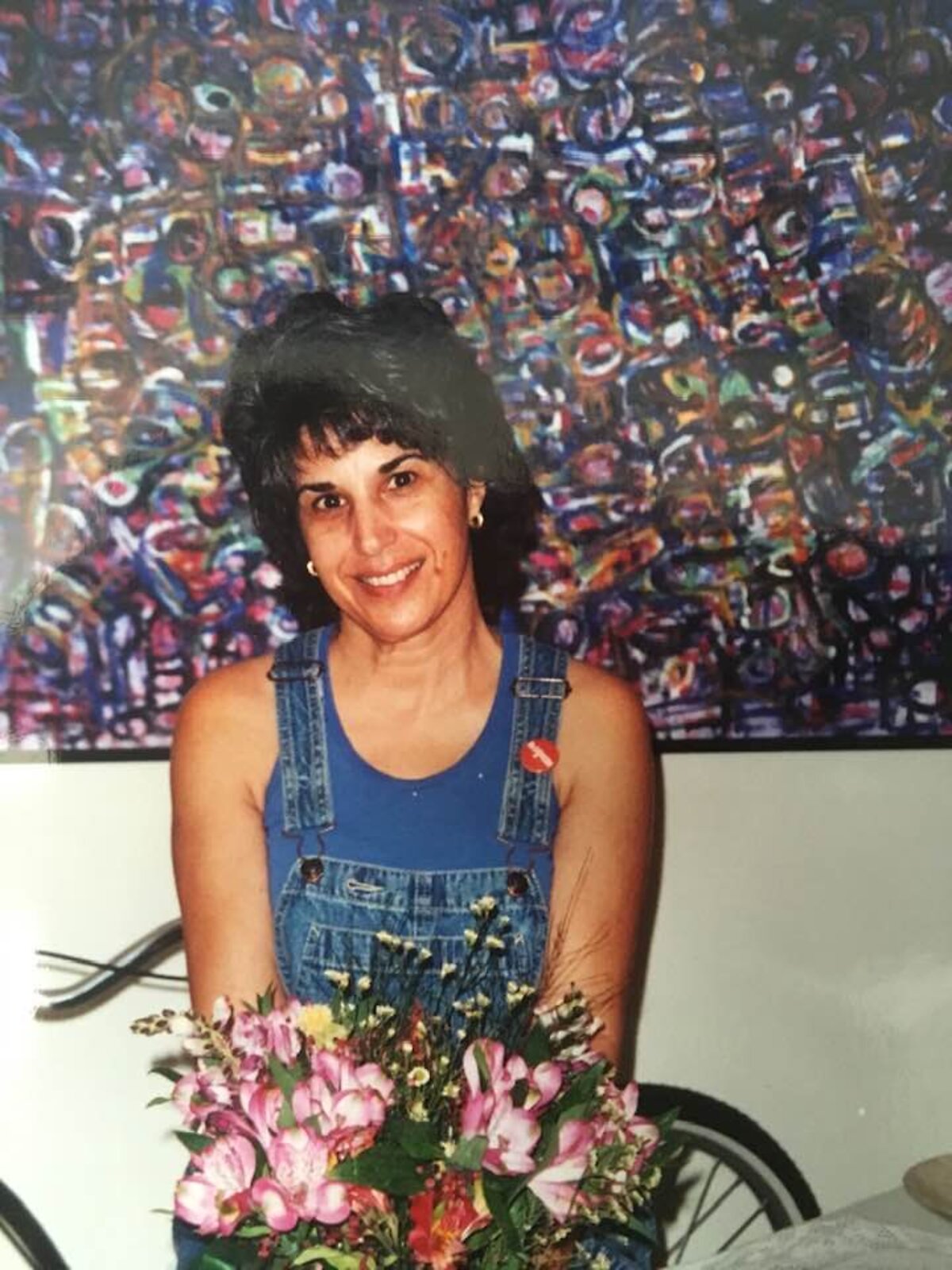 Debra Karen Werner as a younger woman, holding flowers in front of one of her large abstract paintings